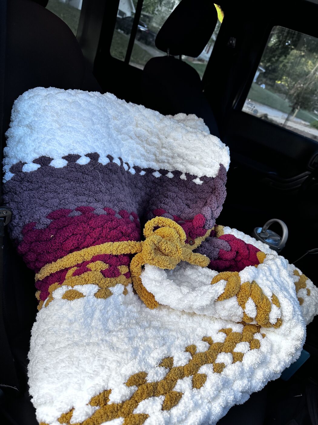Rolled cream, maroon, and gold chunky blanket tied with a bow